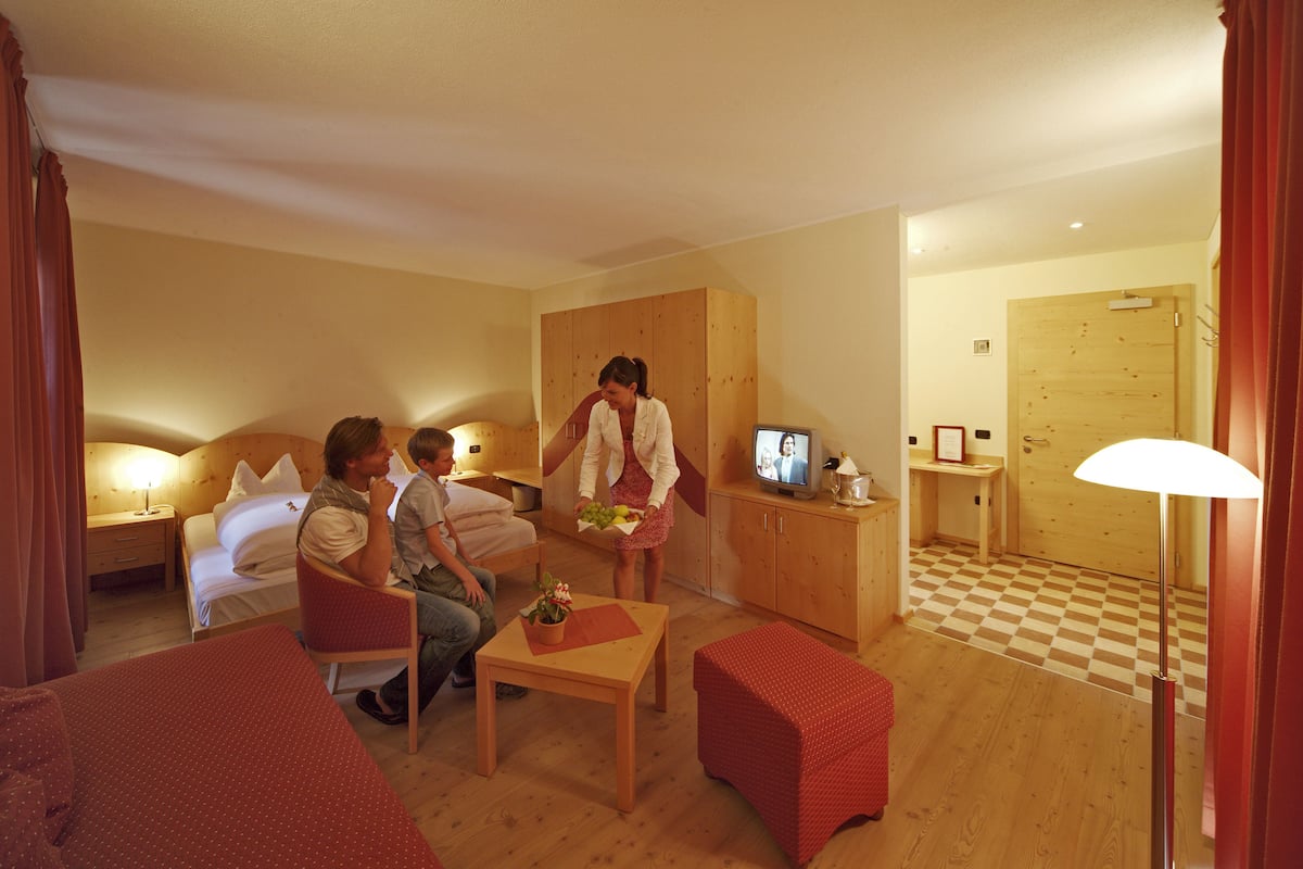 A hotel room with a bed, a desk, a chair, a TV, and a wooden wardrobe.