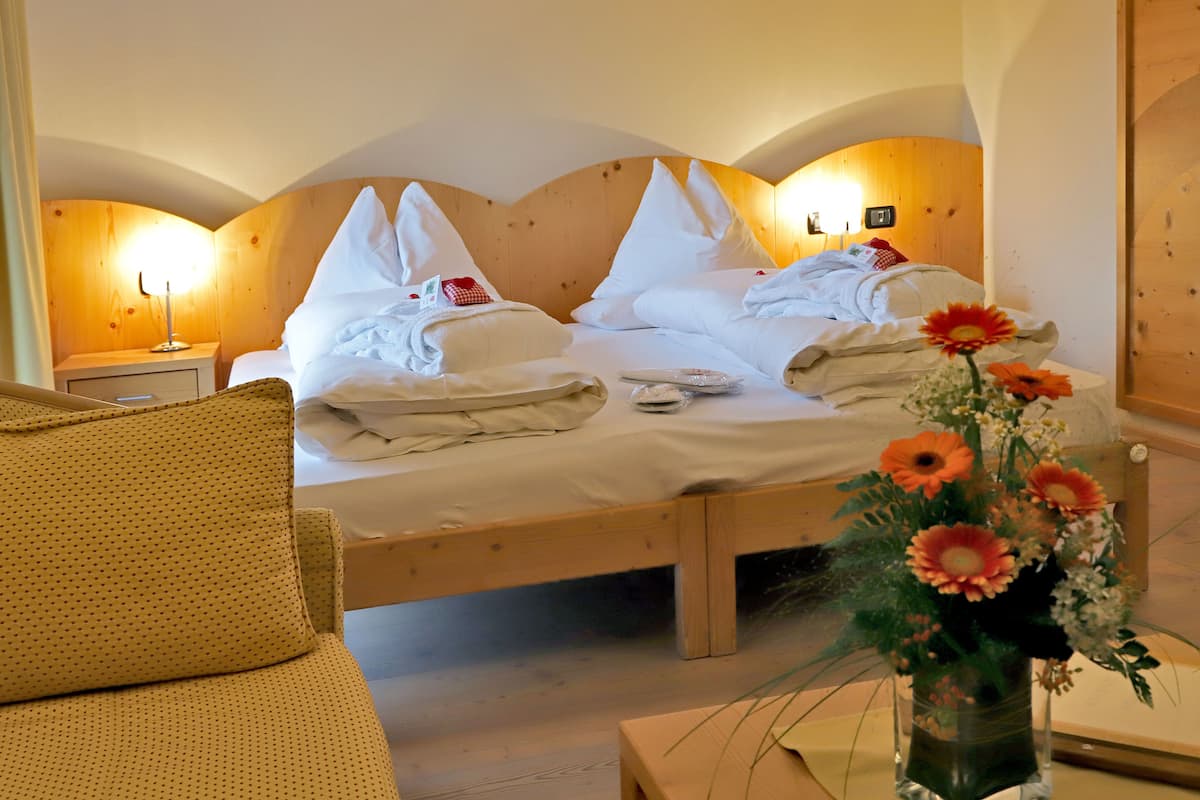 A hotel room with a wooden bed, two bedside tables, a nightstand, and a vase with flowers.