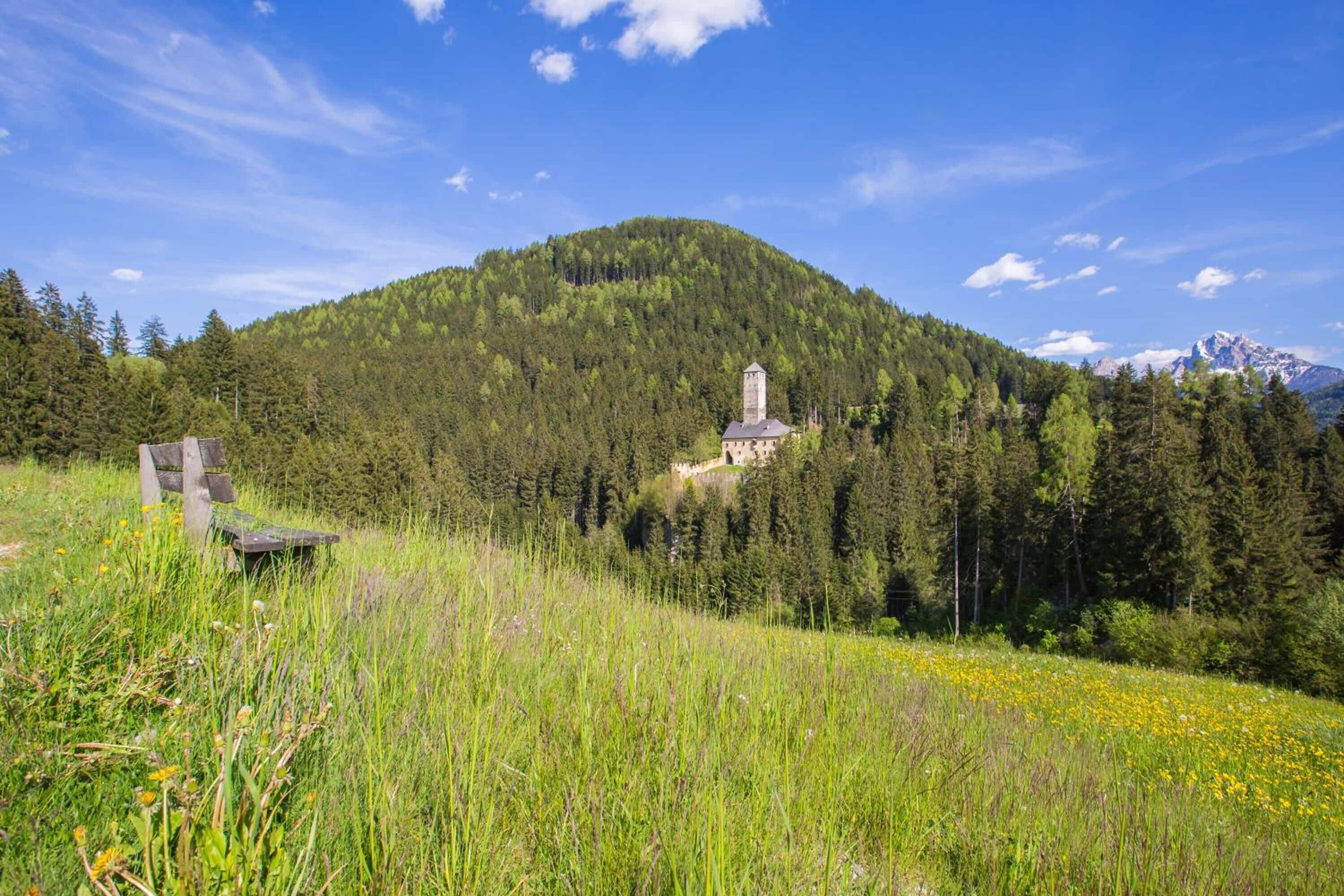 Un paisaje montañoso con una iglesia en una colina, rodeado de un bosque denso y un cielo despejado.