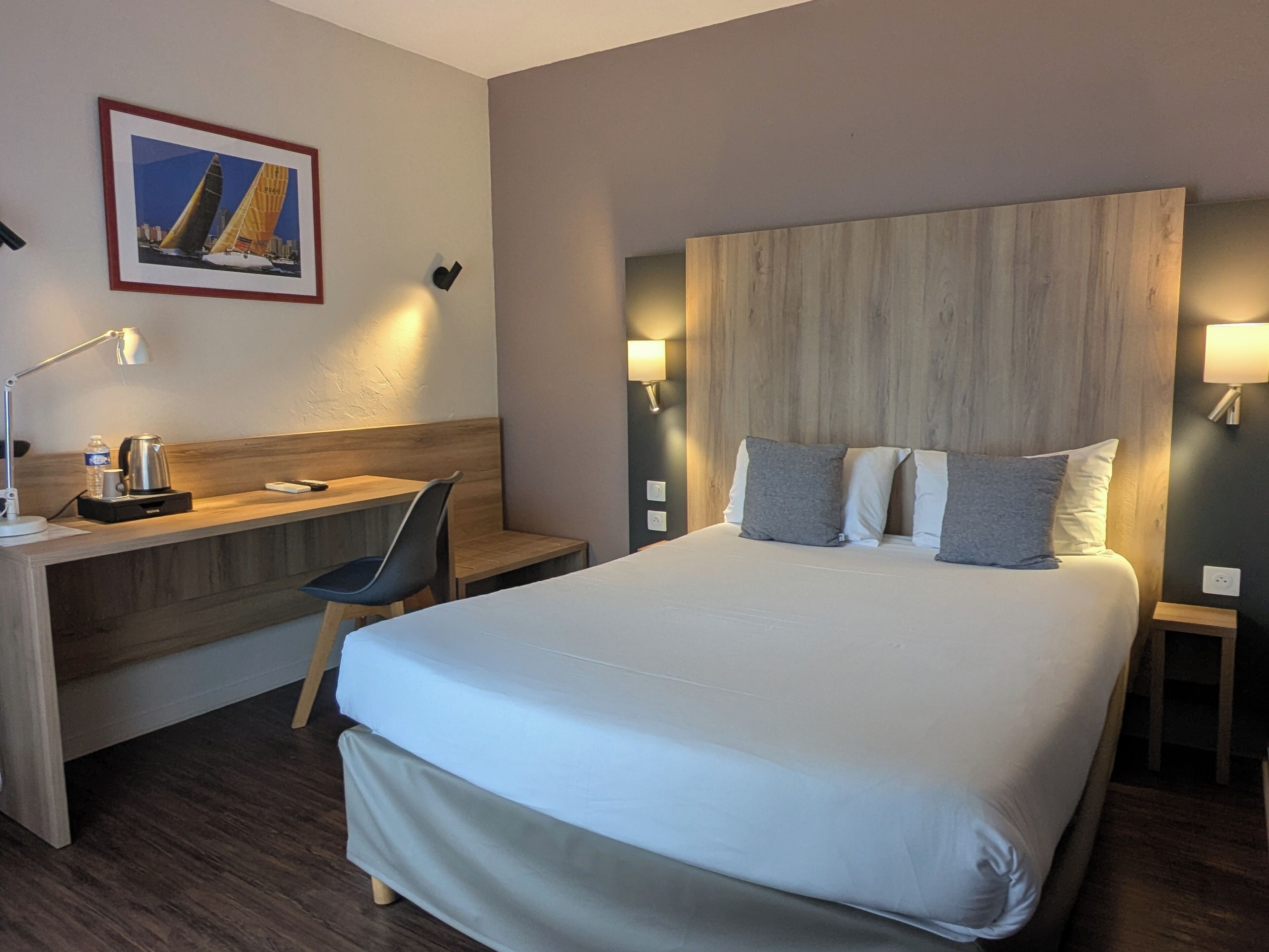 Habitación de hotel con una cama grande, un escritorio, una silla y una mesita de noche con lámpara.