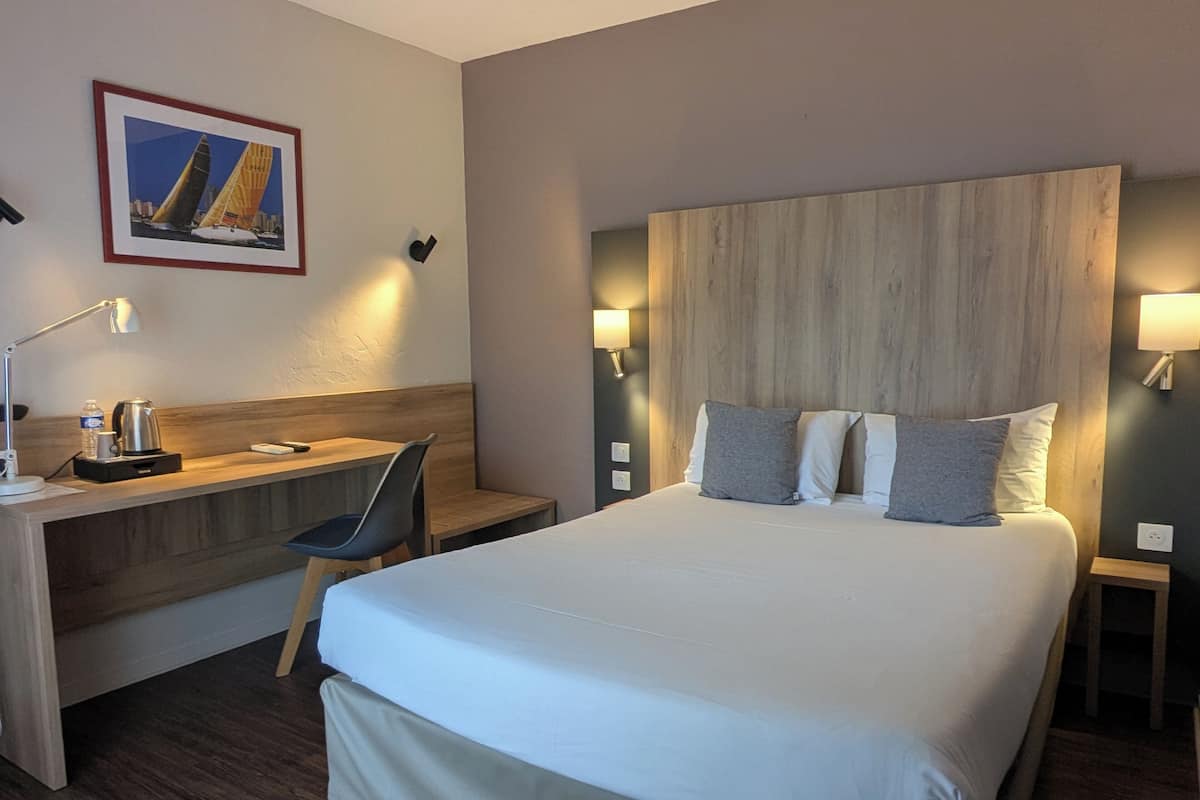 Une chambre d’hôtel avec un grand lit, un bureau, une chaise et une table de chevet avec une lampe.