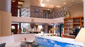 A modern bar area with a mural of a beach scene, a seating area with a white sofa and bar stools, and a collection of glassware on shelves. - The Originals City, Hôtel Le Sextant (Labege)