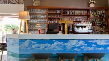 Uma área de bar com um mural representando o céu e o oceano, prateleiras com garrafas de bebidas alcoólicas, uma máquina de café e uma televisão.