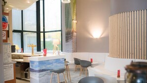 A modern bar area with a counter, stools, and a large window. - The Originals City, Hôtel Le Sextant (Labege)