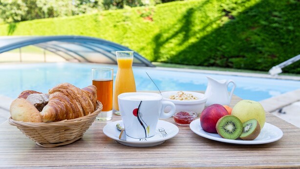 A breakfast setting with croissants, juice, coffee, cereal, and fruit by a pool. - The Originals City, Hôtel Le Sextant (Labege)