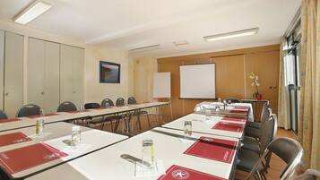 Uma sala de conferências com mesas, cadeiras, um quadro branco e uma tela de projeção.