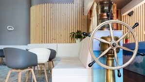 A modern interior with a white sofa, two chairs, a wooden slatted wall, and a brass ship's wheel. - The Originals City, Hôtel Le Sextant (Labege)