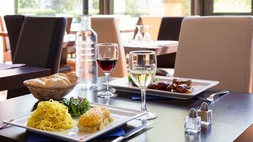 A dining table with plates of spaghetti and a baked dish, two glasses of wine, and salt and pepper shakers.