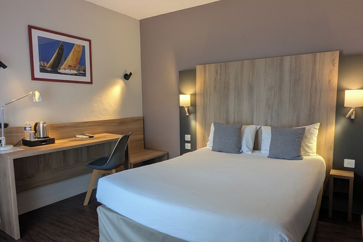 Een hotelkamer met een groot bed, een bureau, een stoel en een nachtkastje met een lamp.