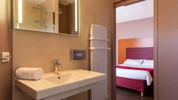 A hotel bathroom with a sink, mirror, and shower.