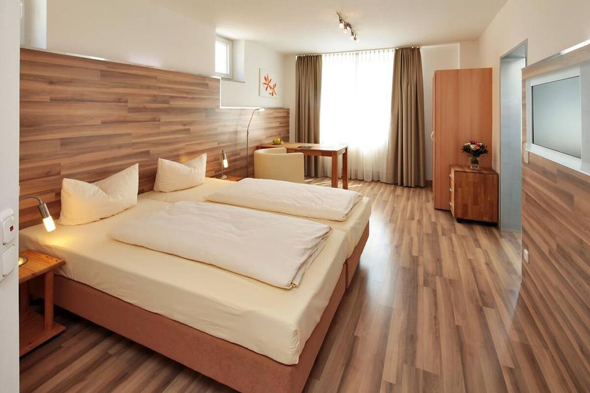 Habitación de hotel con dos camas, un escritorio, una silla, un televisor y un cabecero de madera.