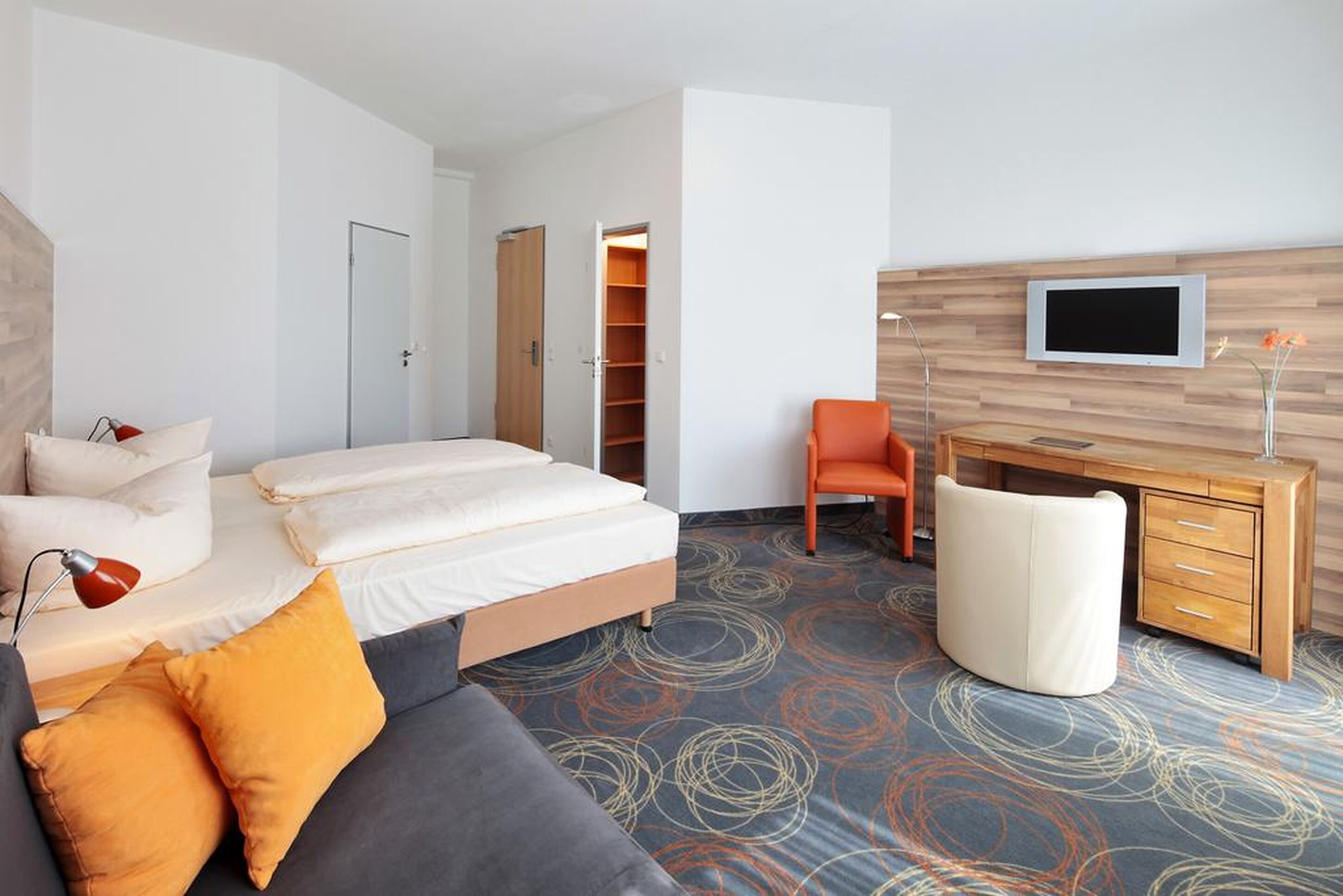 A modern hotel room with a bed, a sofa, a desk, and a TV.