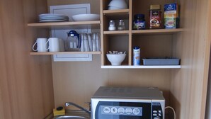 A compact kitchenette with a microwave, sink, and storage shelves. - Petul Apart Hotel Residenz (Essen)