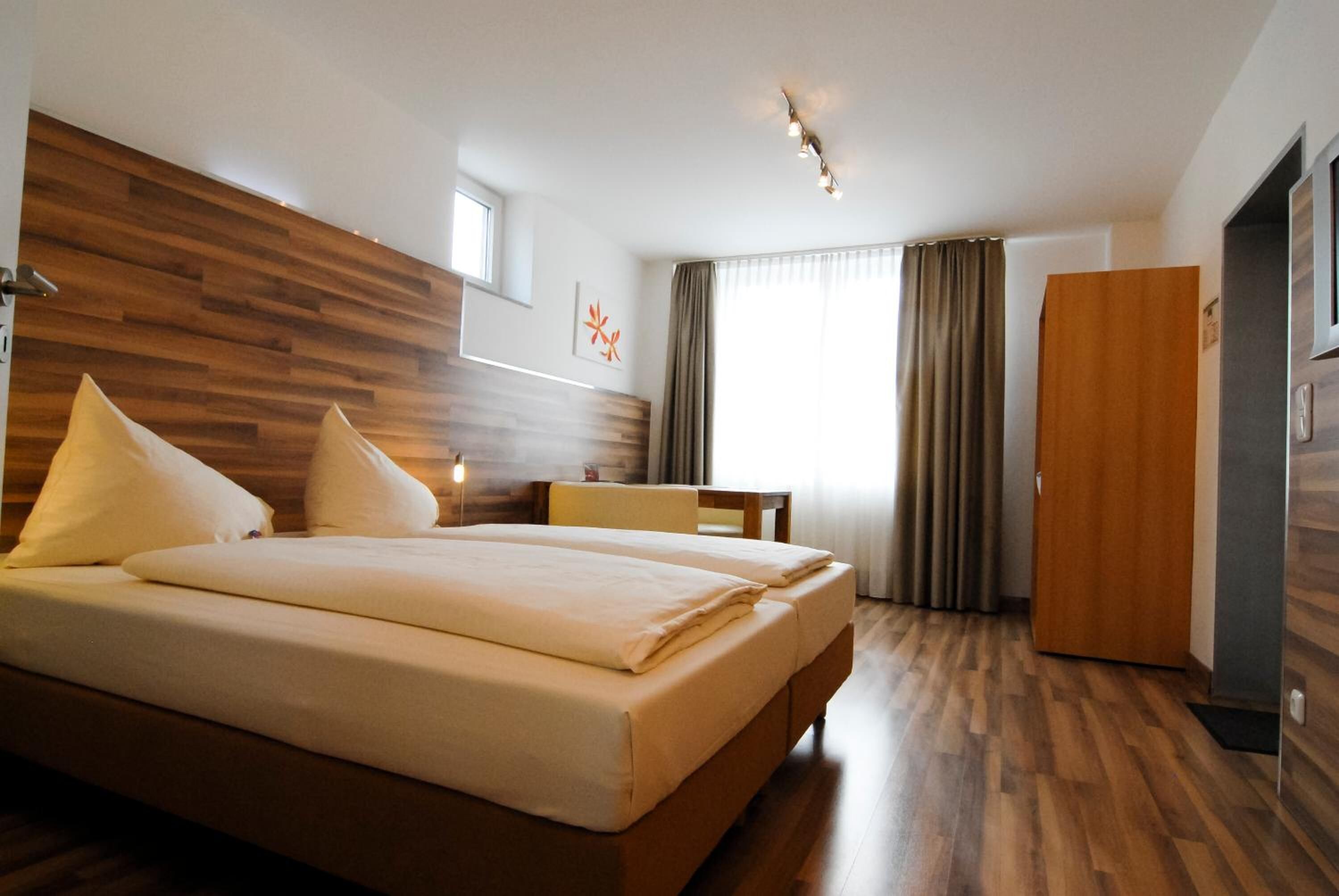 Una habitación de hotel moderna con una cama grande, un cabecero de madera, un escritorio y un armario.