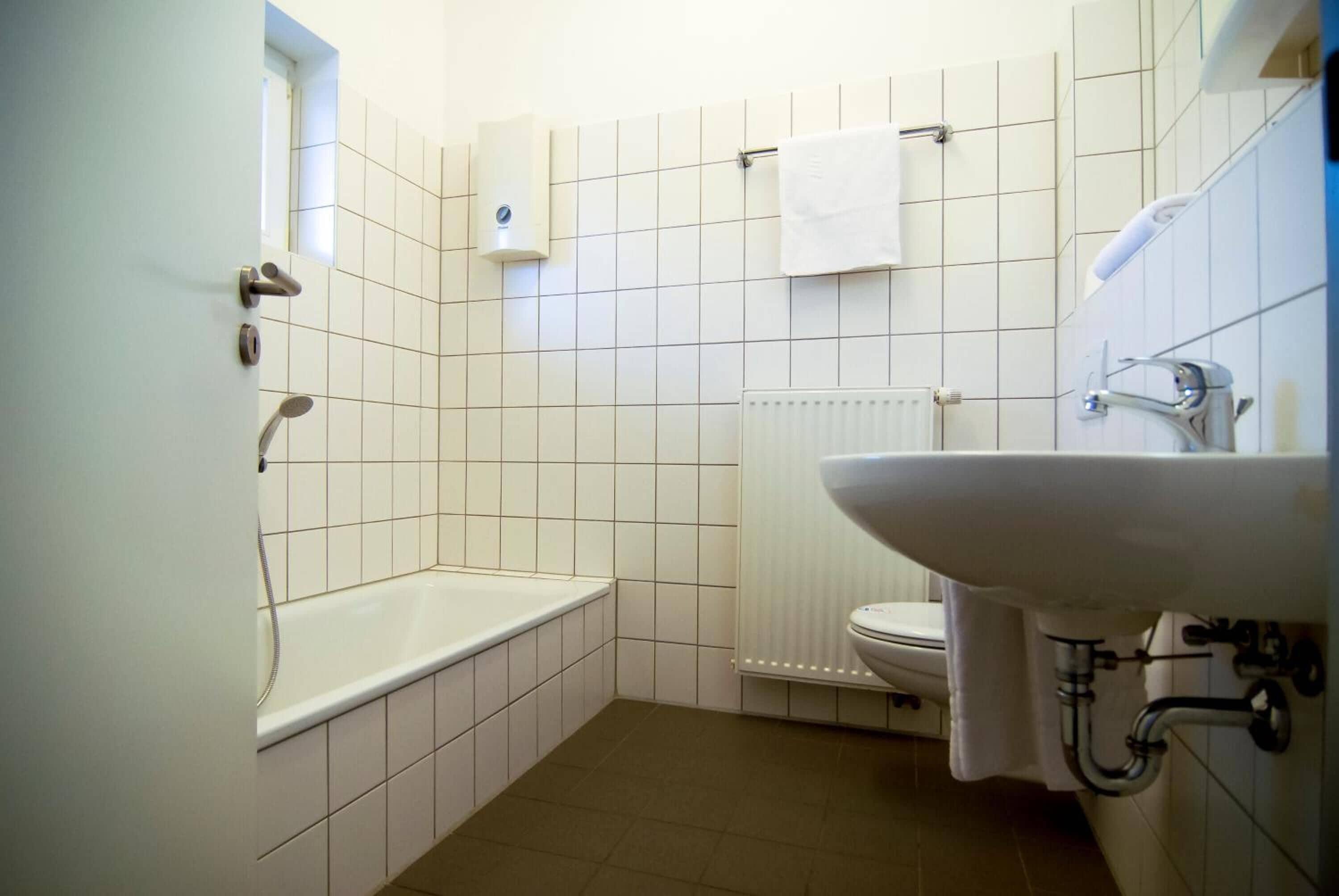 Une petite salle de bain propre, avec des carreaux blancs, une baignoire, des toilettes et un lavabo.