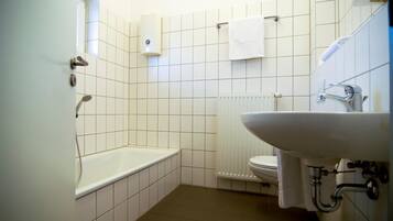 Une petite salle de bain propre, avec des carreaux blancs, une baignoire, des toilettes et un lavabo.