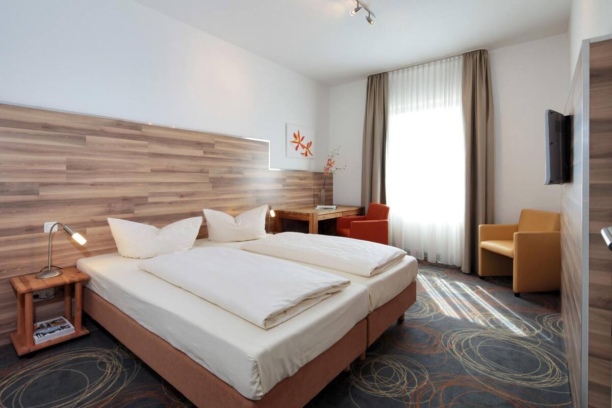 Una habitación de hotel con una cama grande, un escritorio, una silla, un televisor y una ventana con cortinas.