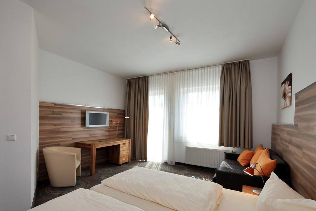 Habitación de hotel con cama, escritorio, silla, televisión y ventana con cortinas.
