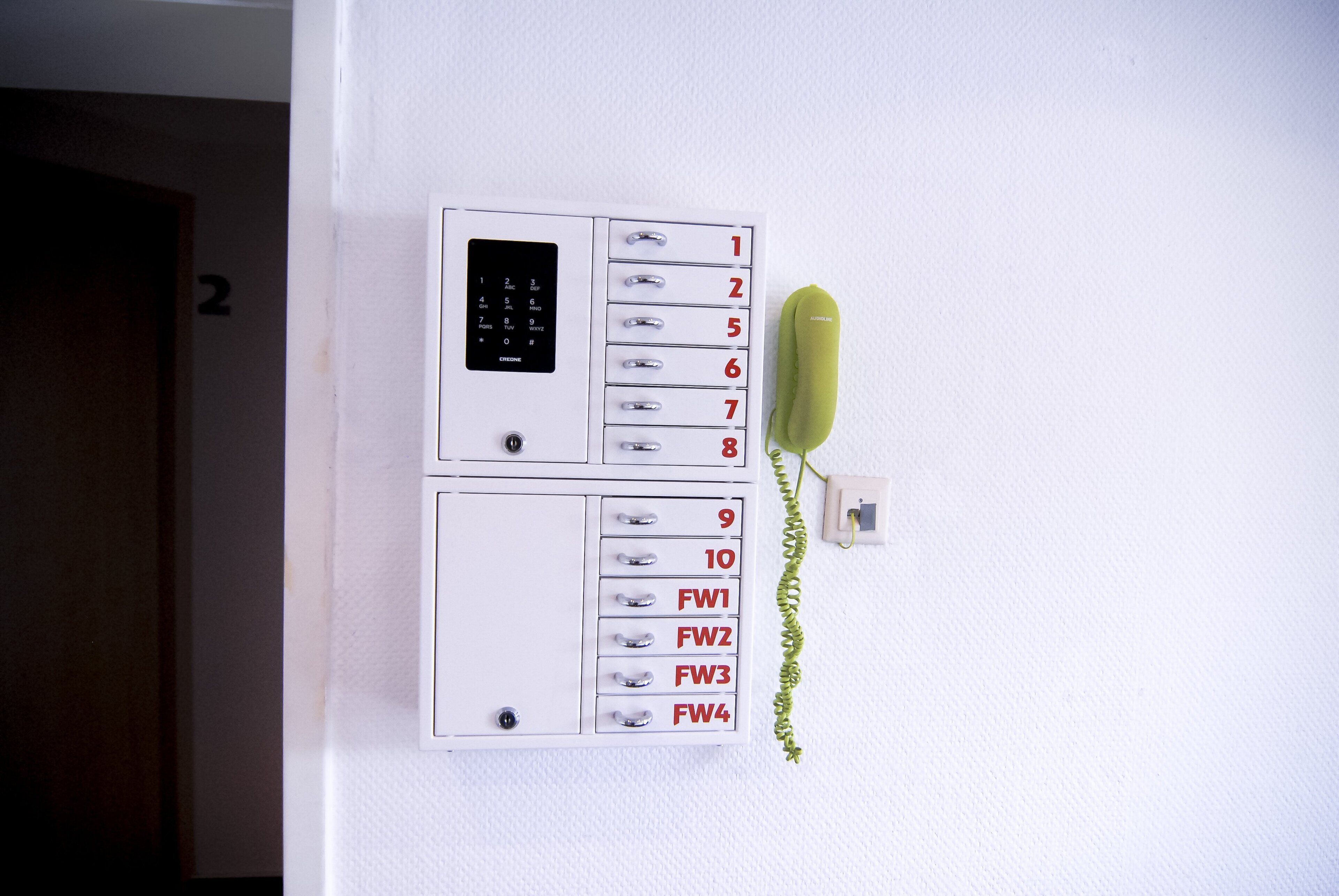 A wall-mounted intercom system with numbered buttons and a green handset.