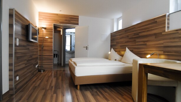 A modern hotel room with a wooden floor, a bed, a desk, and a TV. - Petul Apart Hotel Residenz (Essen)