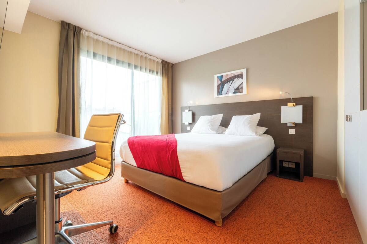 A hotel room with a bed, a chair, a table, and a nightstand.