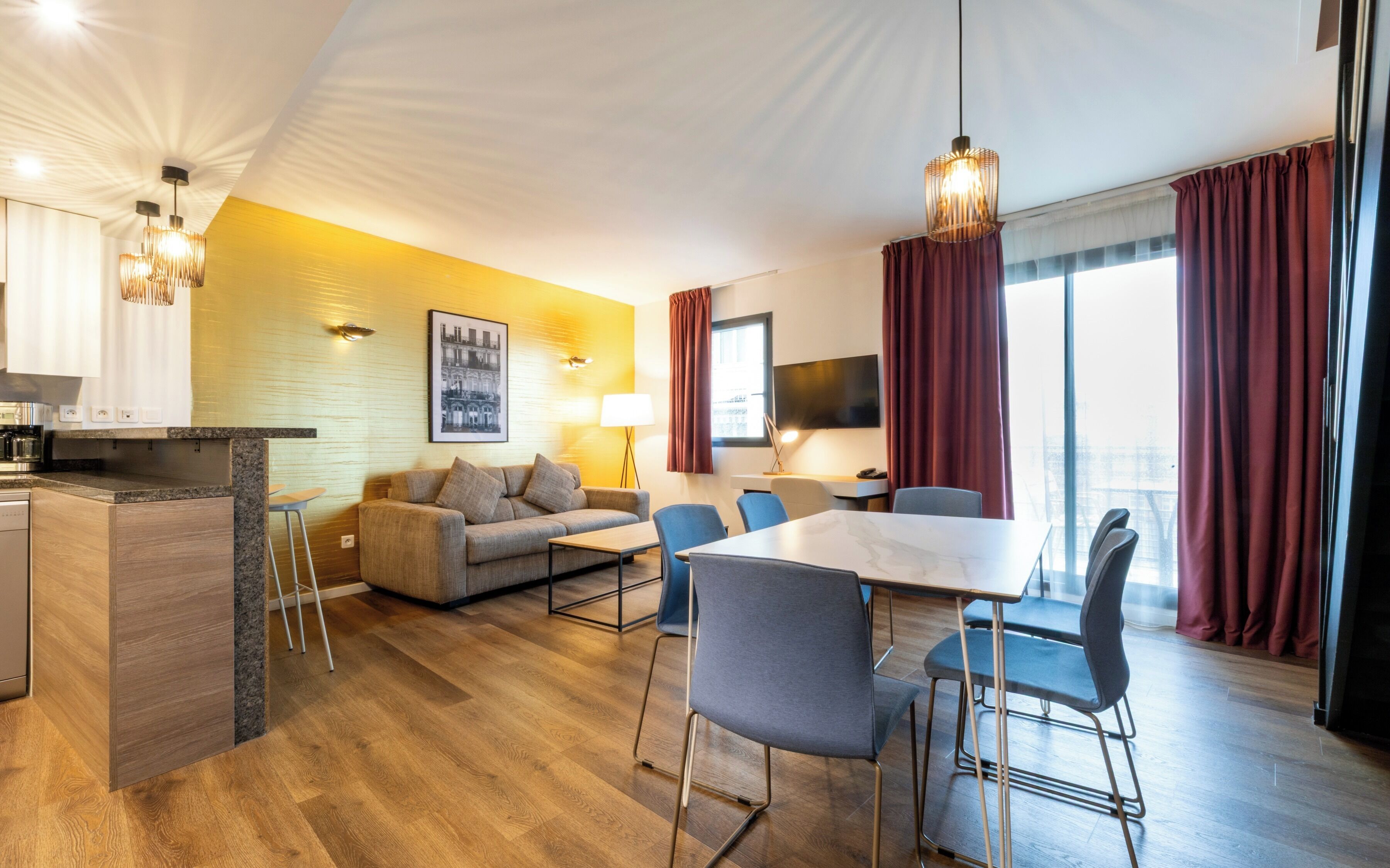 A modern hotel room with a dining area, a sofa, a TV, and a kitchen.