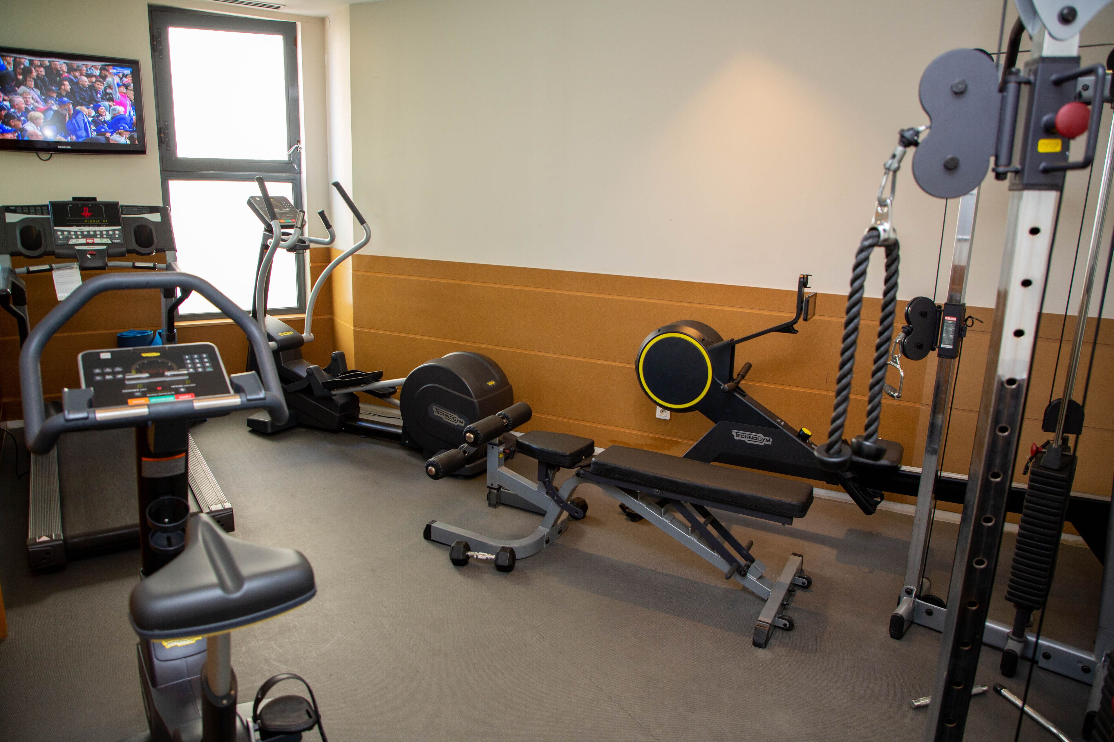 Un gimnàs amb màquines cardiovasculars, equipament de musculació i una pantalla de televisió.