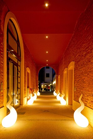 Un couloir aux murs de briques, doté d’arcades et éclairé par des luminaires en spirale.