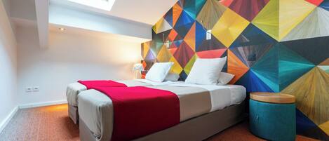 A modern bedroom with a geometric-patterned wall, a bed with a red blanket, and a skylight.