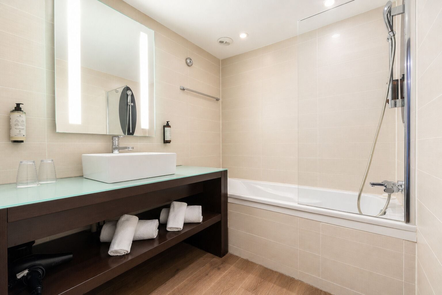 A modern bathroom with a glass countertop, a white sink, a large mirror, a shower, and a towel rack.