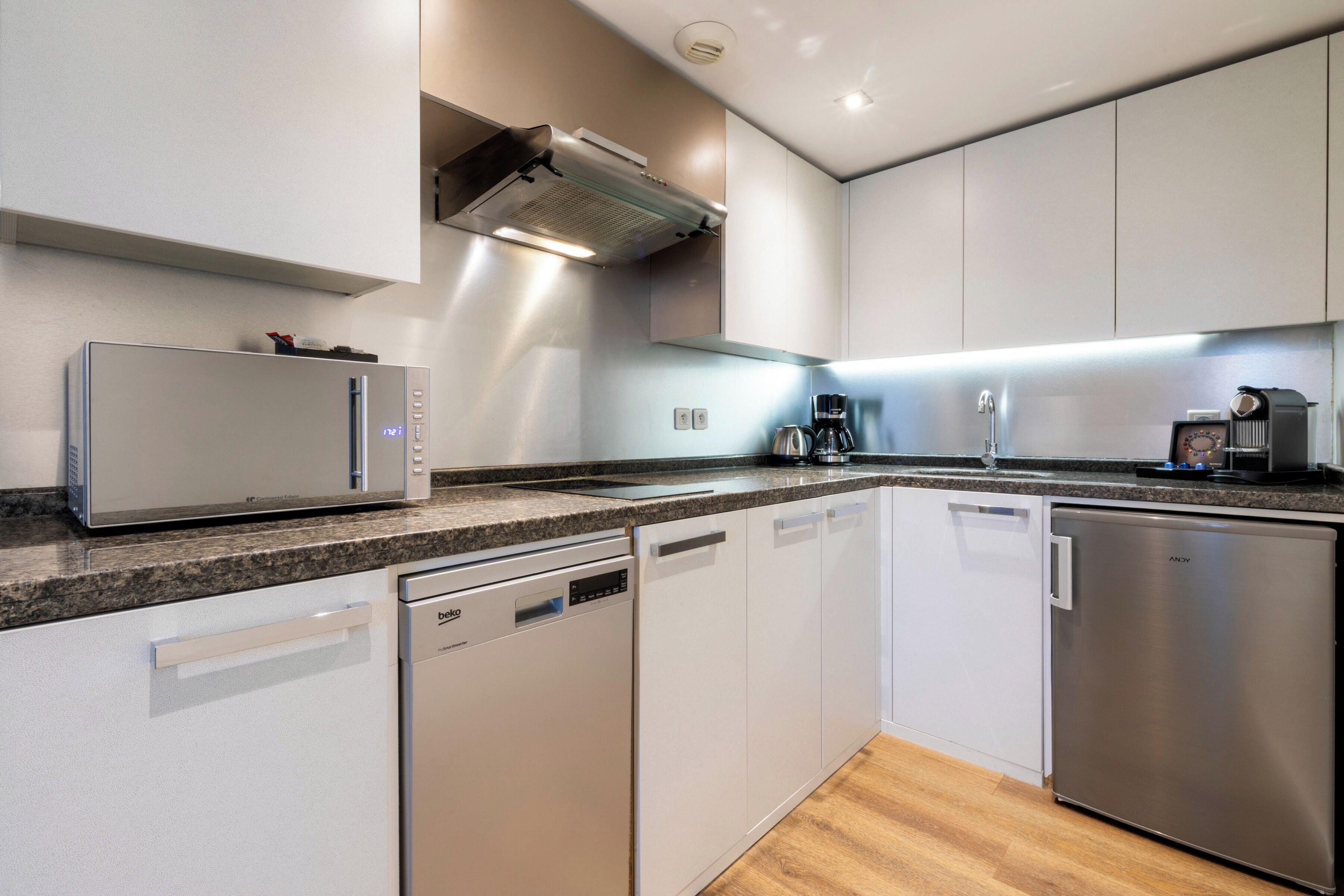A modern kitchen with stainless steel appliances, white cabinetry, and a granite countertop.