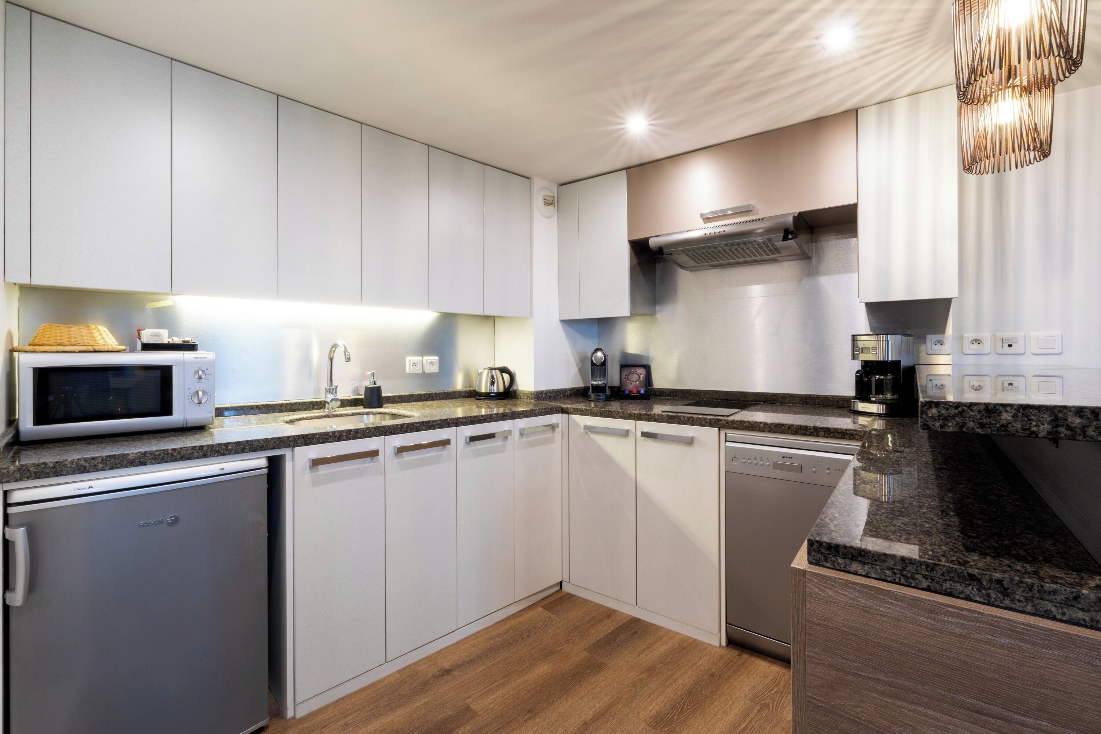 A modern kitchen with white cabinets, a built-in microwave, a coffee maker, and a dishwasher.