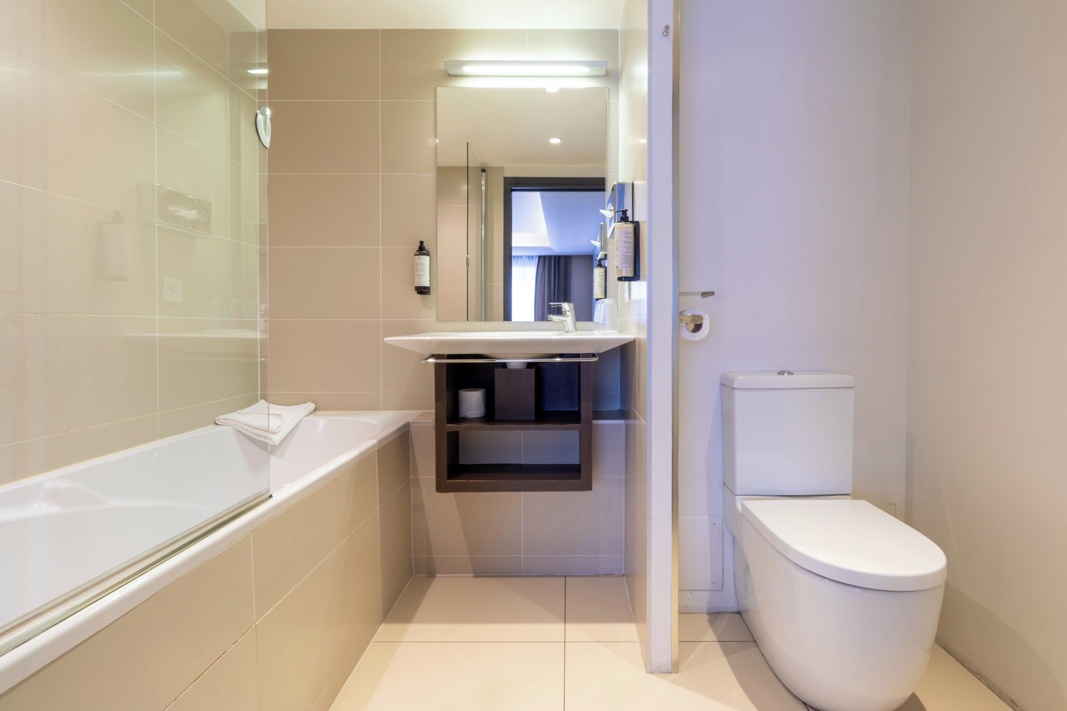 Un baño moderno con bañera, inodoro y espejo sobre el lavamanos.