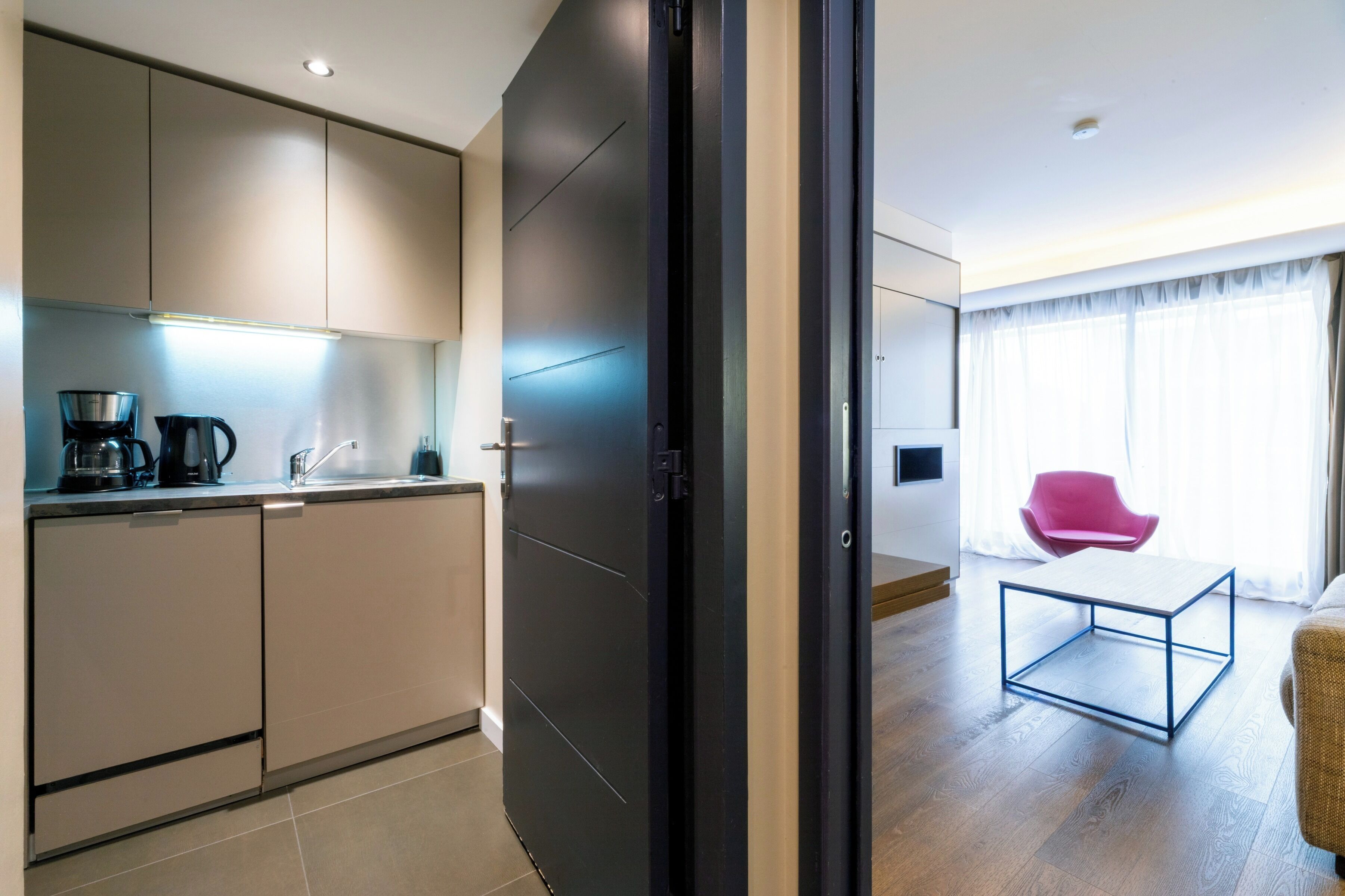 A modern kitchen with a black door, a coffee maker, and a bright window.