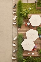 Un patio con piso de madera, varias sillas de descanso y grandes sombrillas.