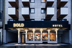 Un hotel llamado "BOLD HOTEL" con una fachada moderna, ventanas grandes y una entrada acogedora.