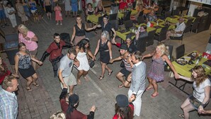 Un espacio al aire libre con mesas y sillas, lleno de gente, rodeado por un muro de ladrillo.