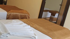 Una habitación de hotel con una cama cubierta con ropa de cama blanca y marrón, una toalla blanca doblada con cuidado sobre la cama y una puerta de madera al fondo.