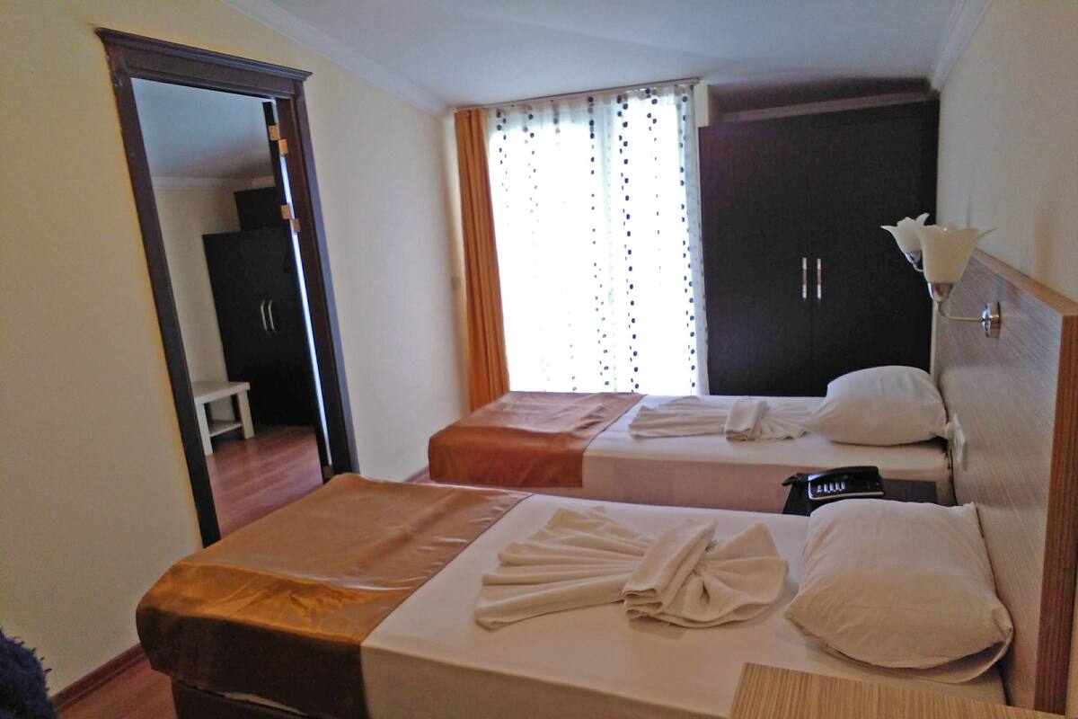A hotel room with two beds, a wardrobe, a bedside table, and a mirror.