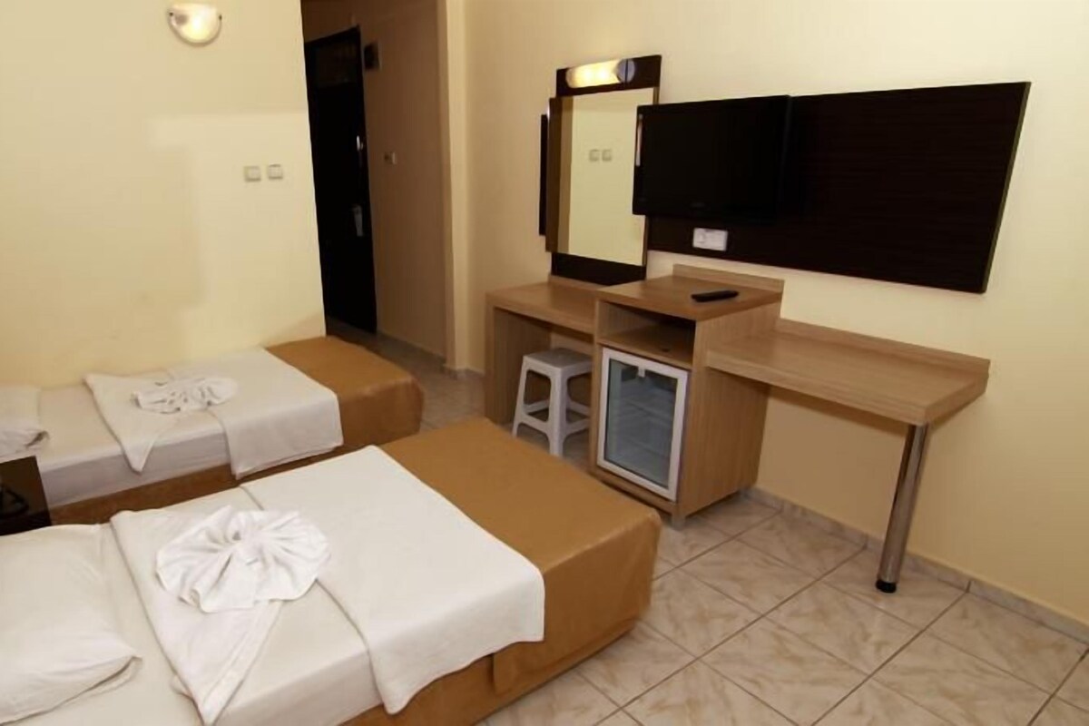 A hotel room with two single beds, a small desk with a mirror, a television, and a refrigerator.