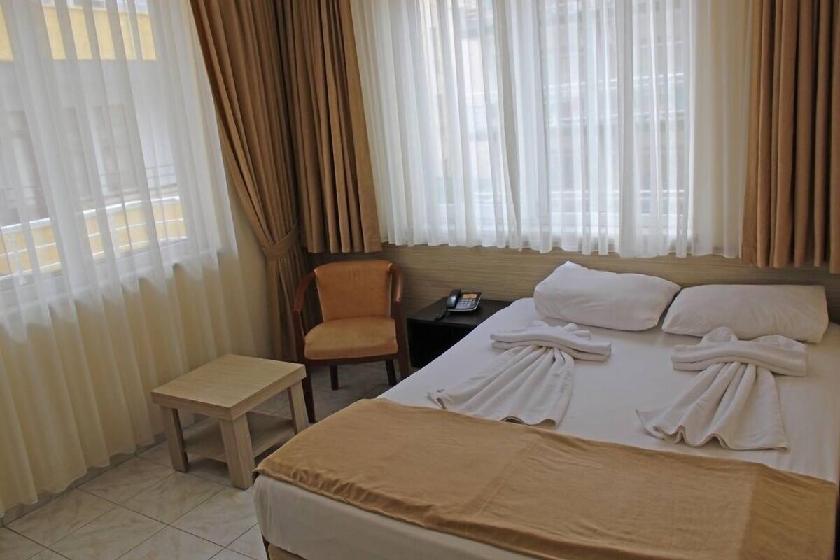 A hotel room with a bed, a chair, a small table, and a window with curtains.