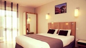 A hotel room with a large bed, a wooden headboard, two bedside lamps, and a cityscape picture on the wall.