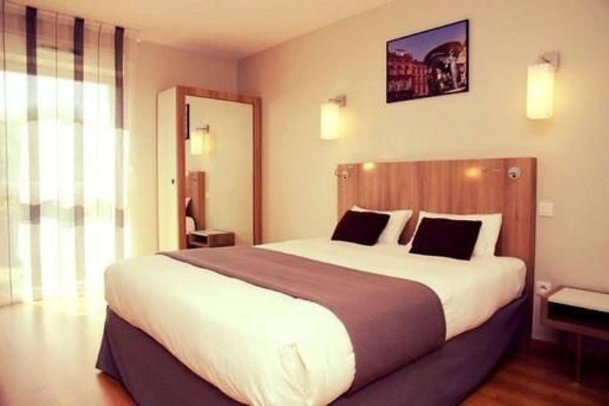 Habitación de hotel con una cama grande, cabecera de madera, dos lámparas de noche y una fotografía de la ciudad en la pared.