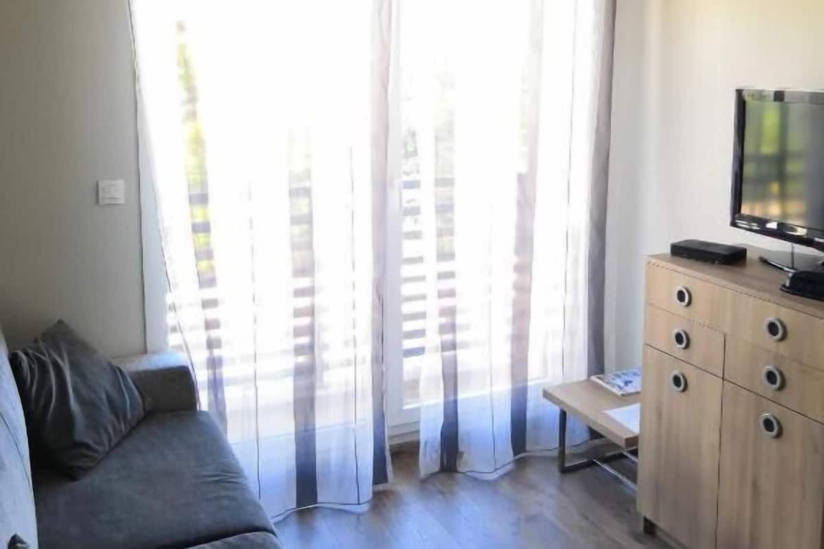 Una sala de estar con un sofá, un televisor sobre un mueble de madera y una ventana con cortinas a rayas.