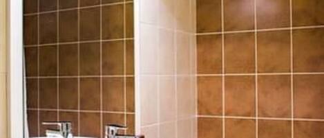 A bathroom with a wooden vanity, a large mirror, and brown tiled walls.