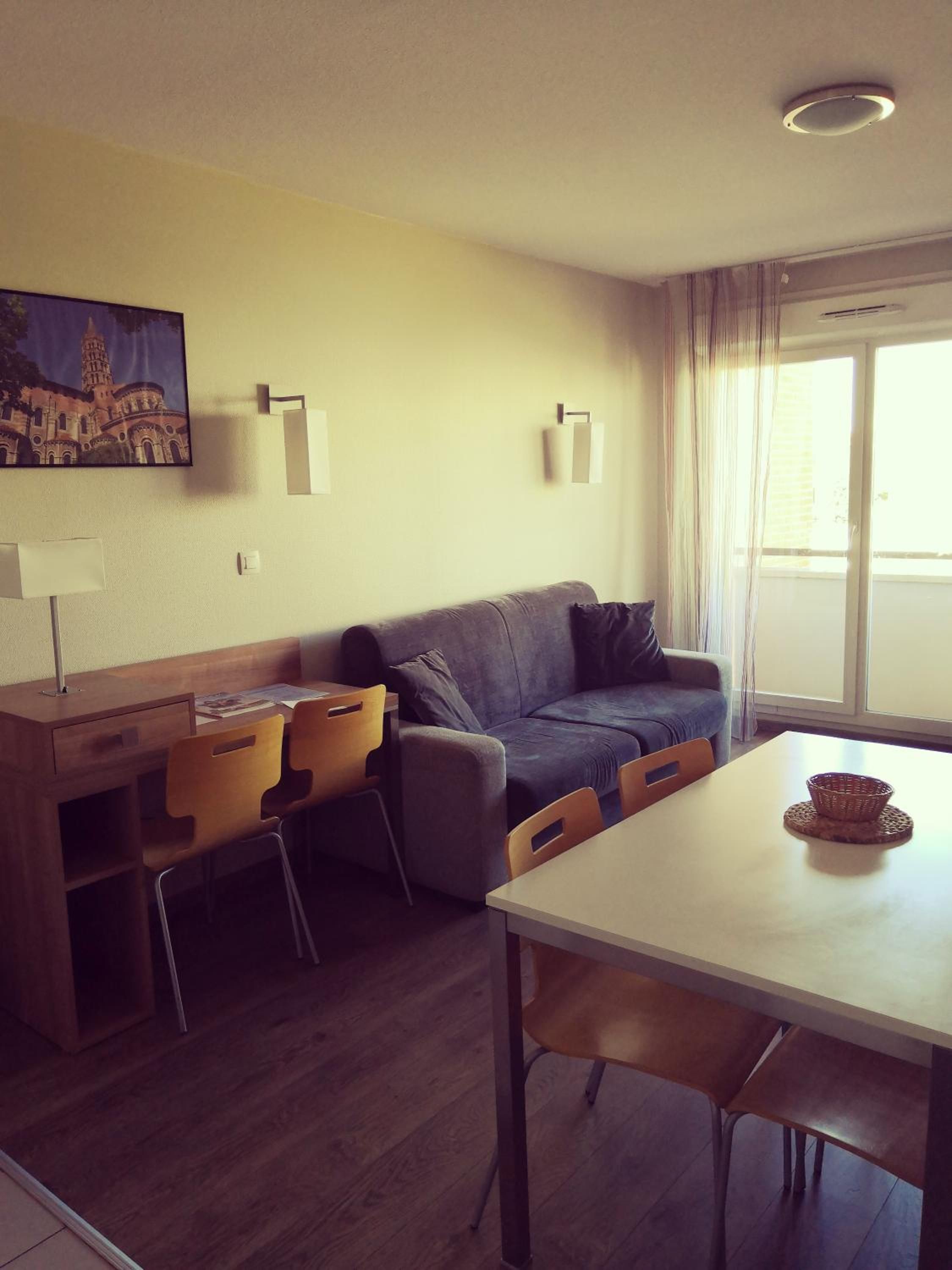 A modern living room with a sofa, chairs, a dining table, and a painting on the wall.
