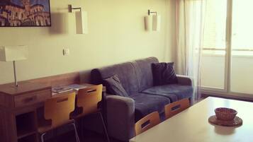 A modern living room with a sofa, chairs, a dining table, and a painting on the wall.