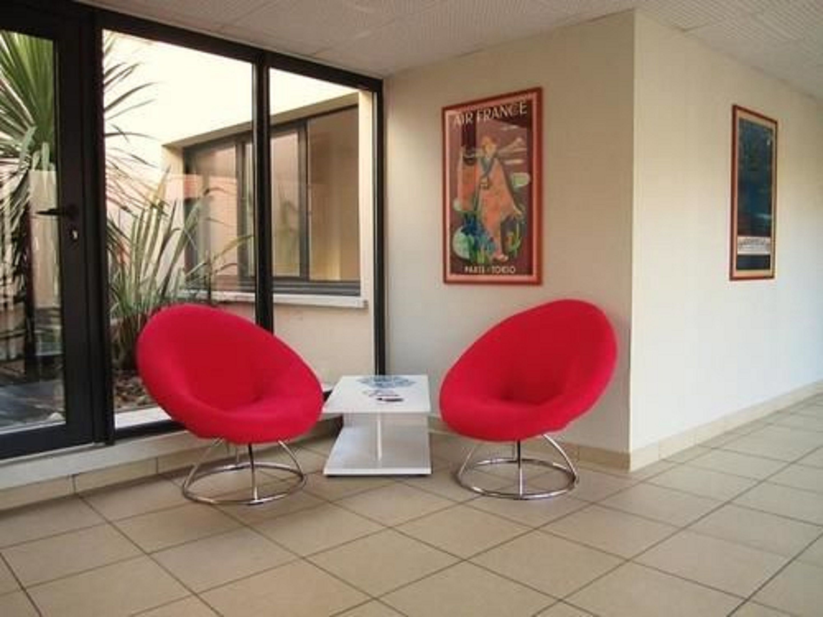 Une pièce avec deux chaises rouges, une petite table et une affiche accrochée au mur.