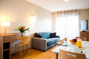 Une chambre d’hôtel moderne équipée d’un canapé, d’une table à manger avec des chaises, d’une télévision et d’une fenêtre avec des rideaux.