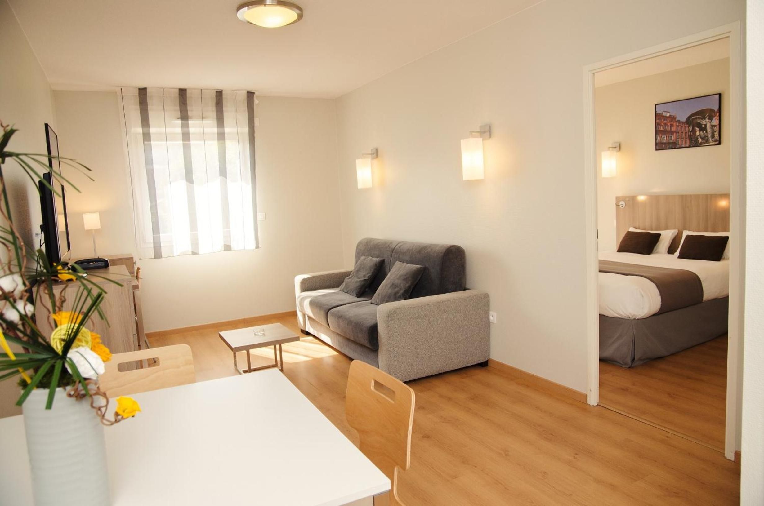 A modern living room with a grey sofa, a small white table, and a dining area.